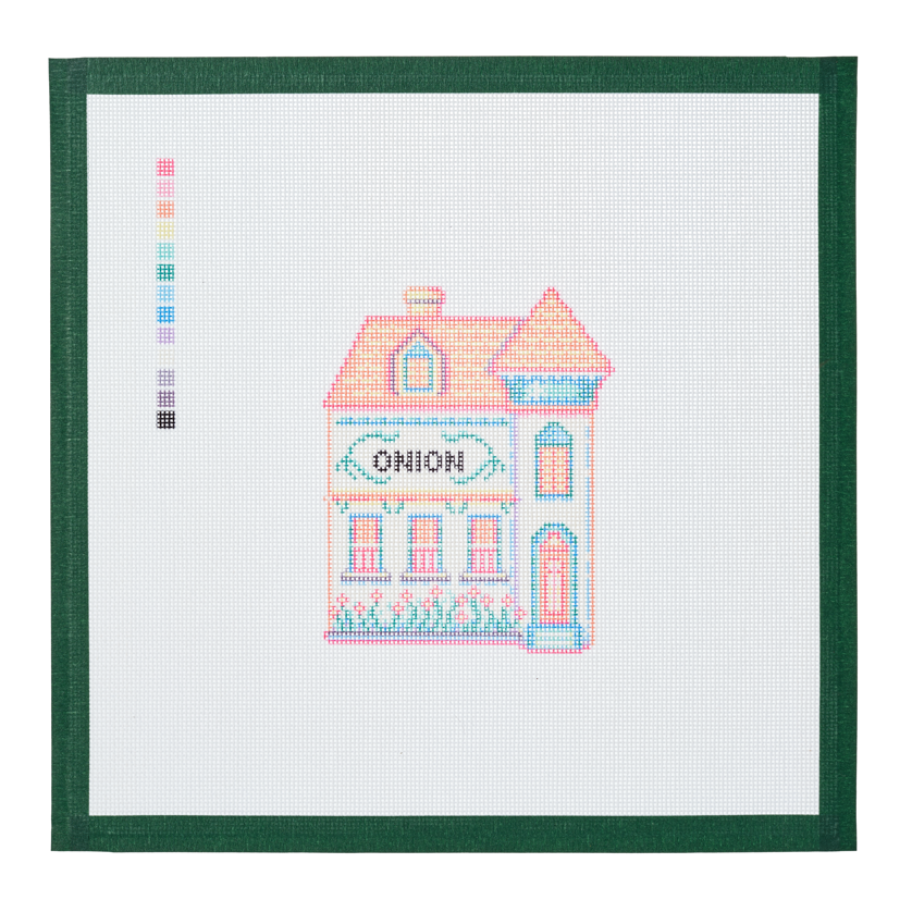 A needlepoint canvas of the Onion house, a small pastel building with its name on the front, on white mesh with a green taped edge.