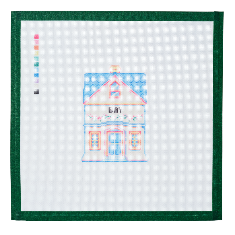 A needlepoint canvas of the Bay house, a small pastel building with its name on the front, on white mesh with a green taped edge.