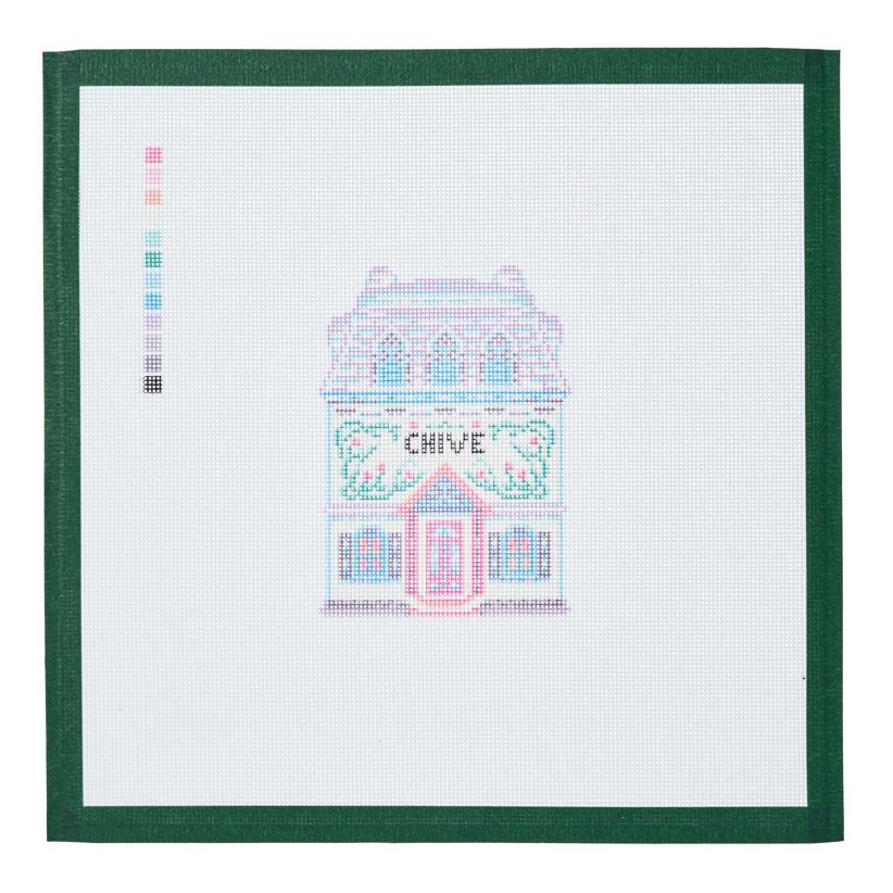 A needlepoint canvas of the Chive house, a small pastel building with its name on the front, on white mesh with a green taped edge.