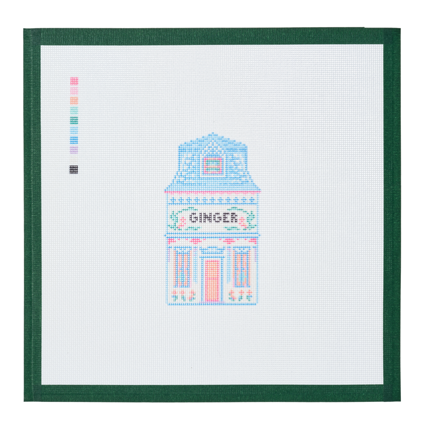 A needlepoint canvas of the Ginger house, a small pastel building with its name on the front, on white mesh with a green taped edge.