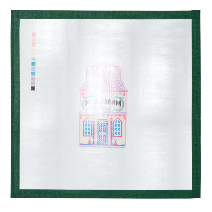 A needlepoint canvas of the Marjoram house, a small pastel building with its name on the front, on white mesh with a green taped edge.