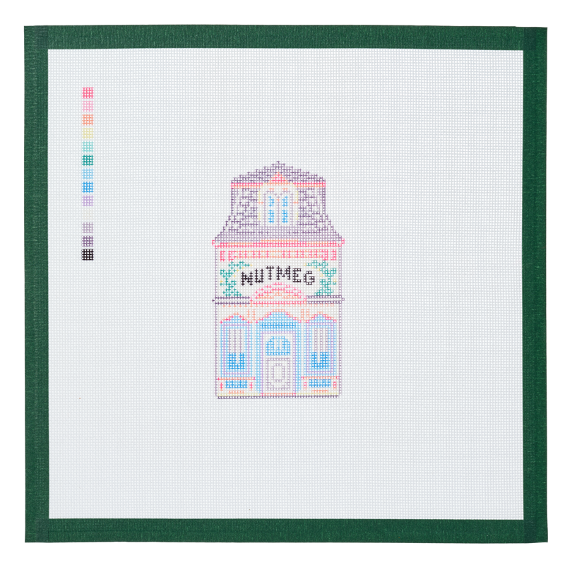 A needlepoint canvas of the Nutmeg house, a small pastel building with its name on the front, on white mesh with a green taped edge.