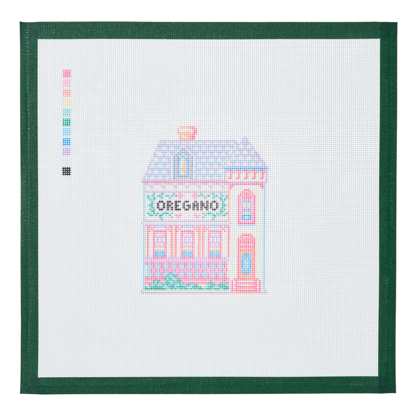 A needlepoint canvas of the Oregano house, a small pastel building with its name on the front, on white mesh with a green taped edge.