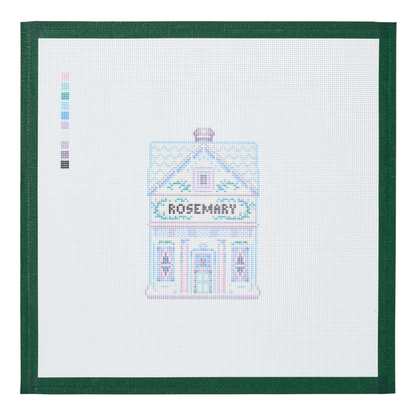 A needlepoint canvas of the Rosemary house, a small pastel building with its name on the front, on white mesh with a green taped edge.