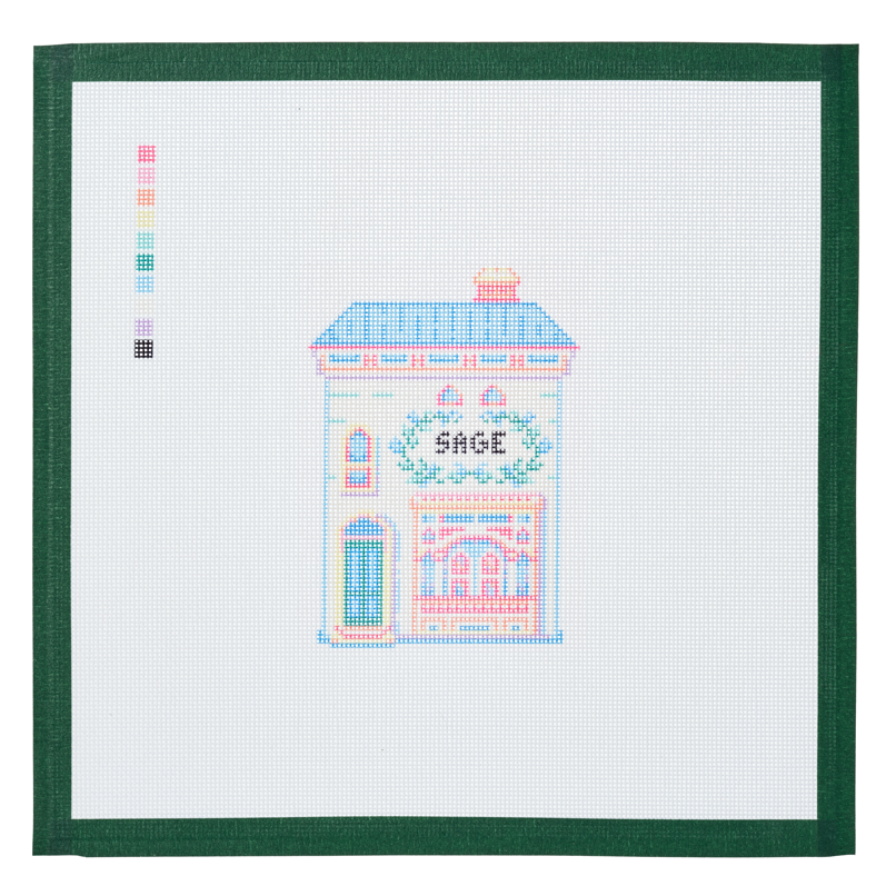 A needlepoint canvas of the Sage house, a small pastel building with its name on the front, on white mesh with a green taped edge.